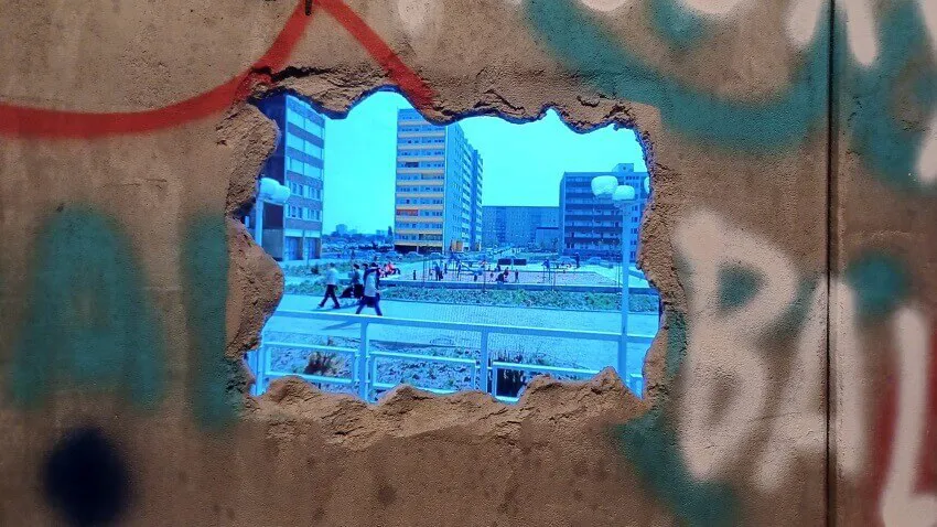 A hole in a wall of graffiti that shows tall buildings and people walking past.
