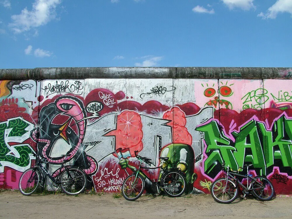 Street art and graffiti on the Berlin Wall as three bicycles lean against the wall.