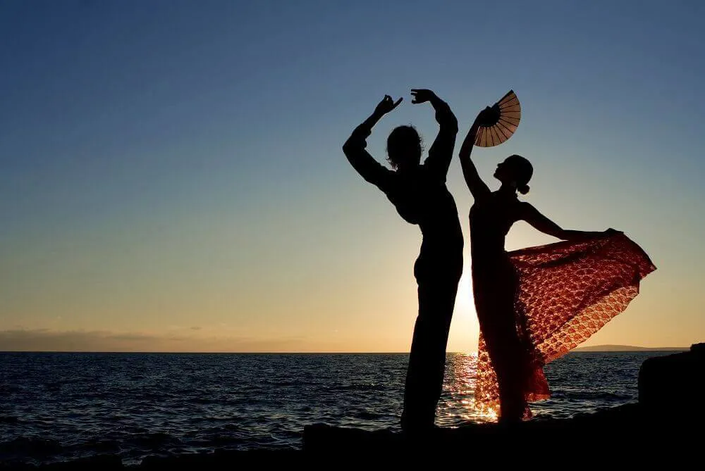 The sun set over the ocean as a man and woman perform authentic flamenco dances.
