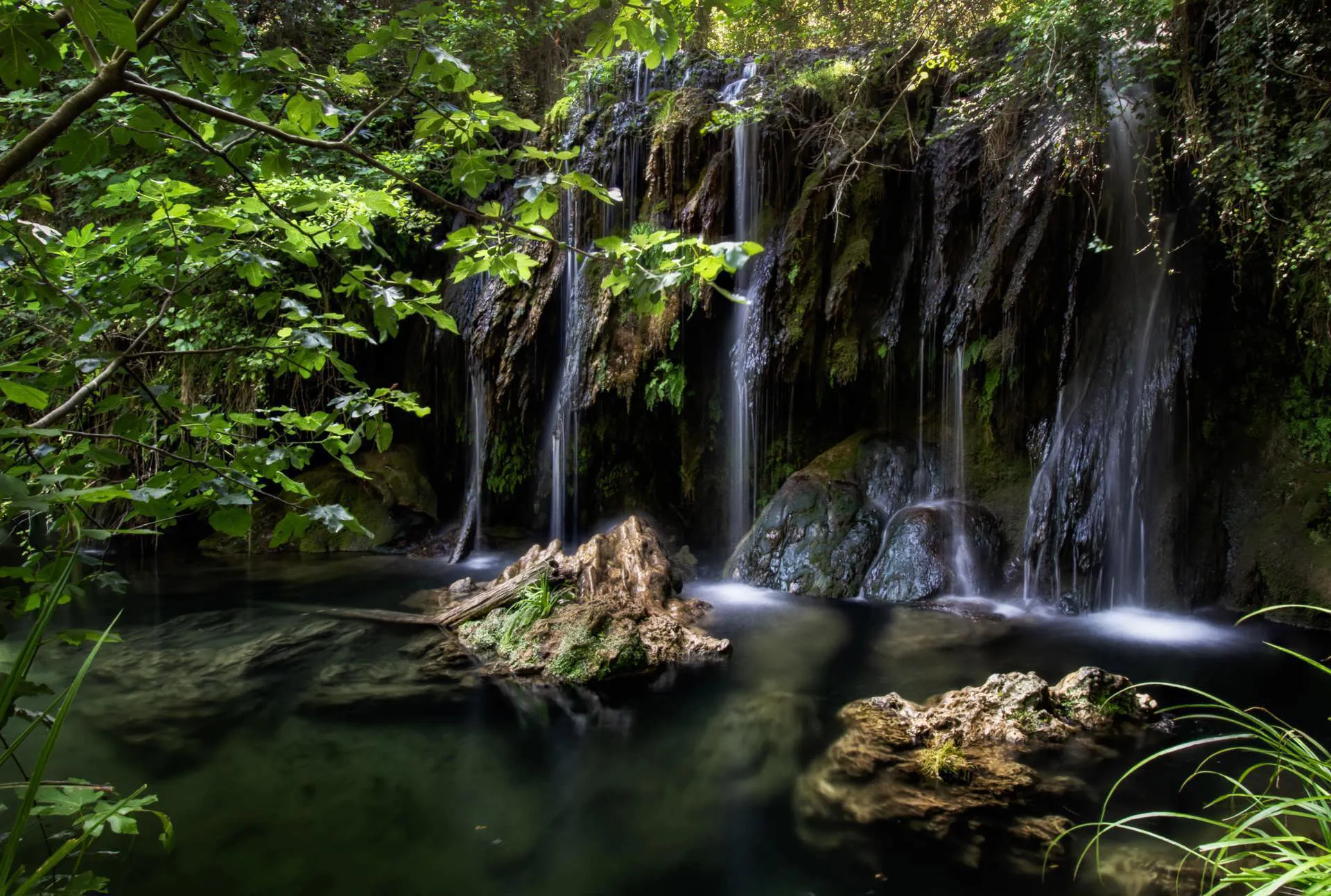 A waterfall, lake, and green trees in La Garrotxa Natural Park.