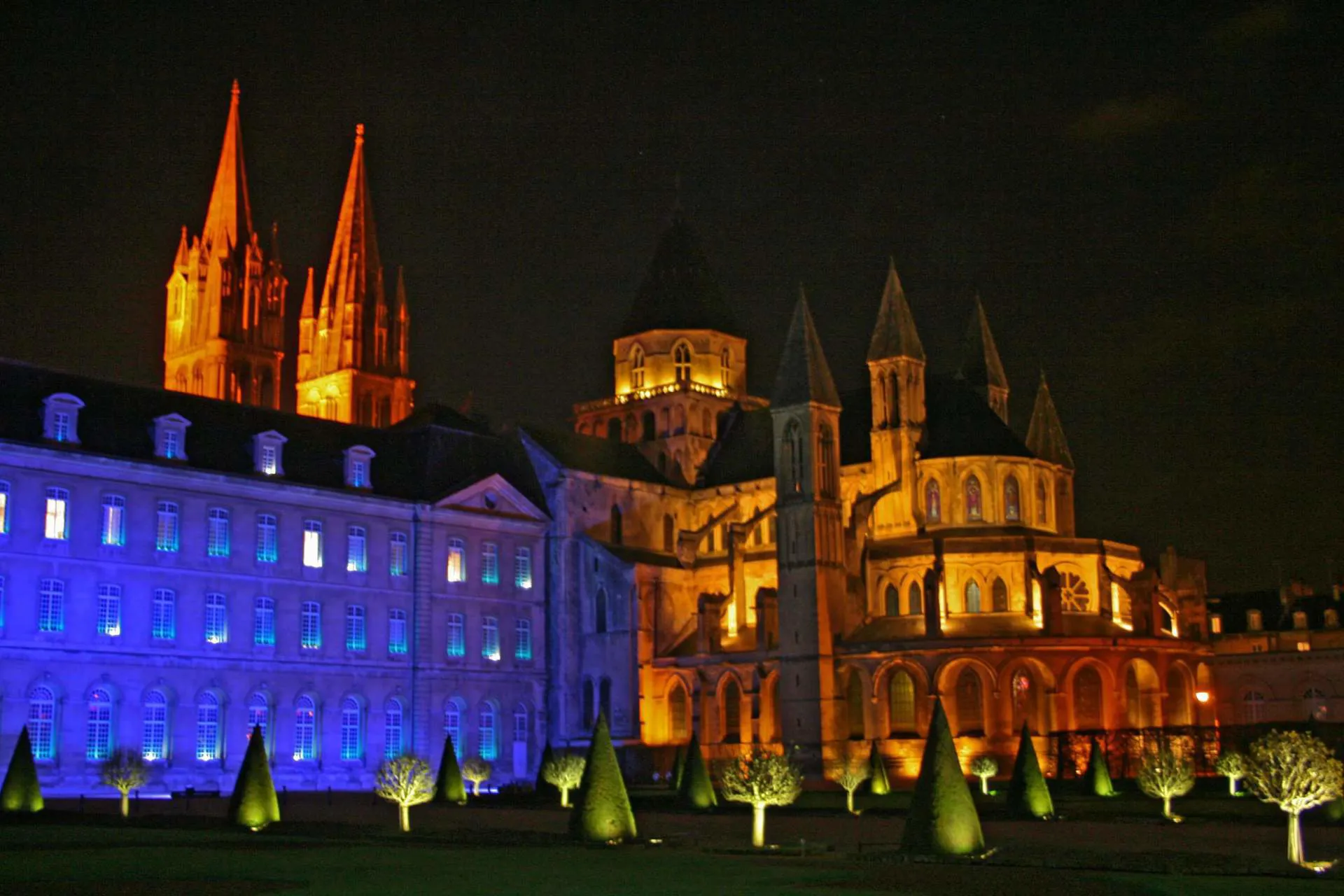 The colourful exterior of the Abbaye aux Hommes illuminated at night.