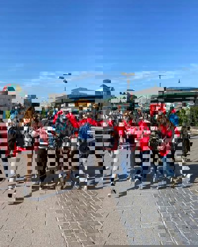 A group of students walking down road, wearing red jackets, with their arms around each other.