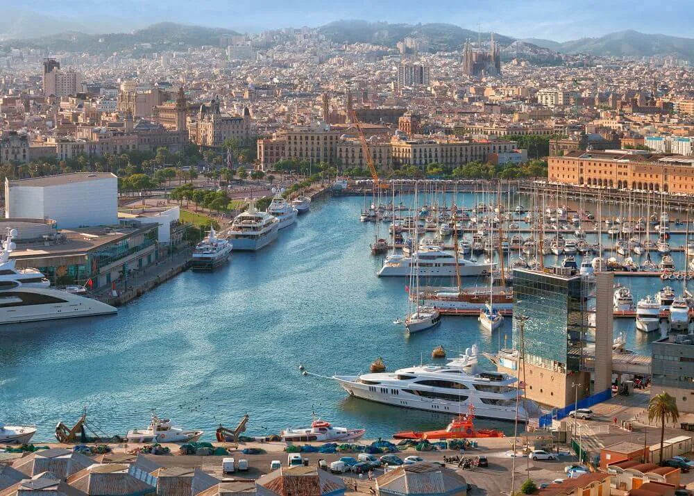 Boats are docked up against a port in Barcelona as the image also shows the rest of Barcelona, Spain.