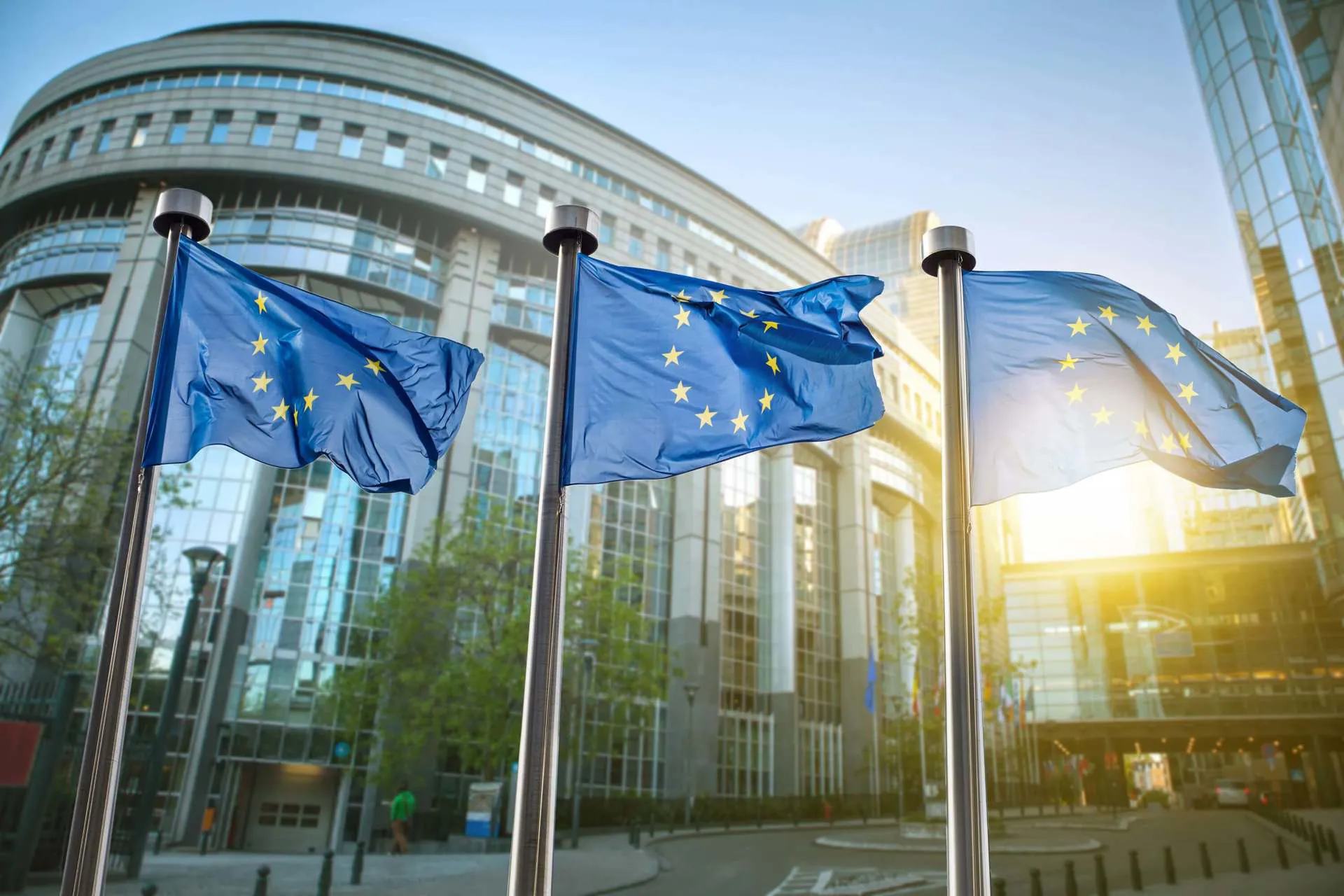 Three European Union flags are dressed on flagpoles outside of the European Parliament.