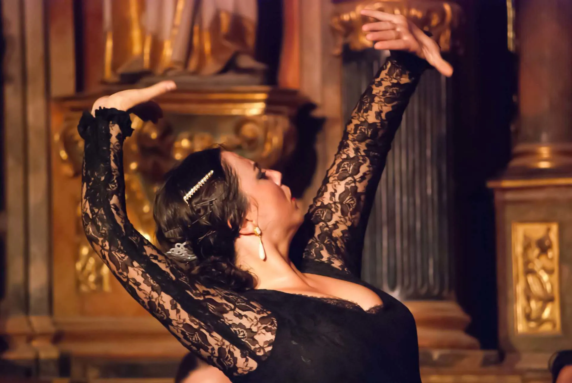 A woman wearing a headpiece and black dress performs authentic flamenco dance.