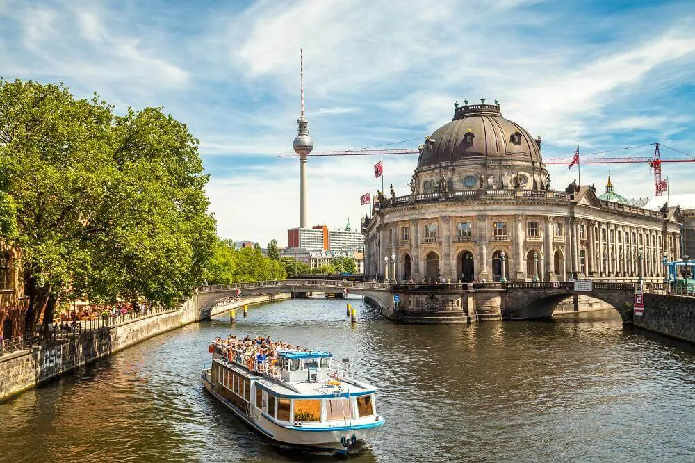 A tourist river boat passes along a river in Berlin, leading up to the Television Tower.