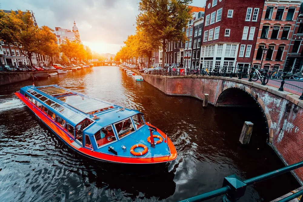A blue and orange canal boats travel on a canal through Amsterdam.