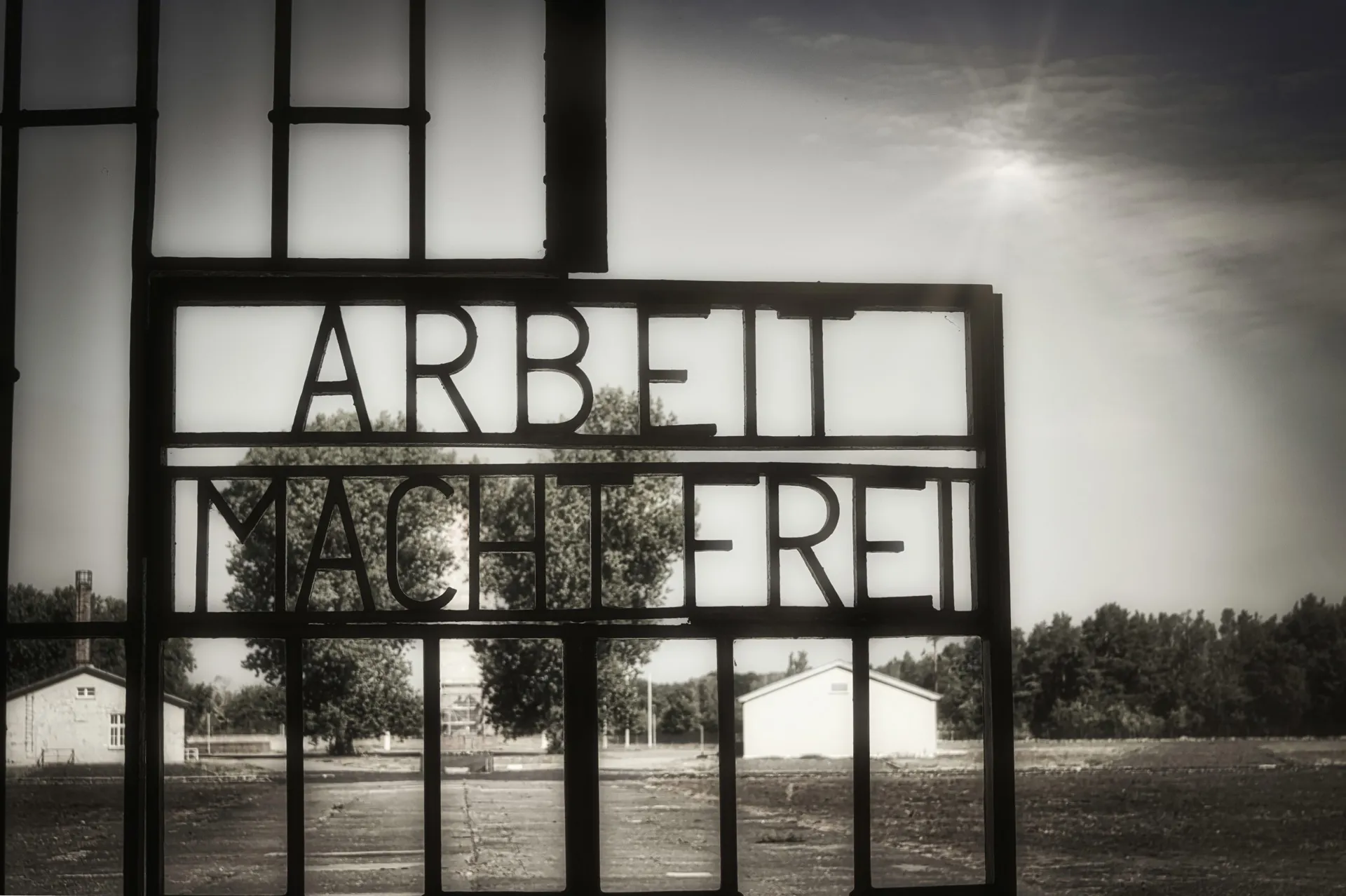 A metal gate reading 'ARBEIT MACHTFREI'  in front two white buildings.