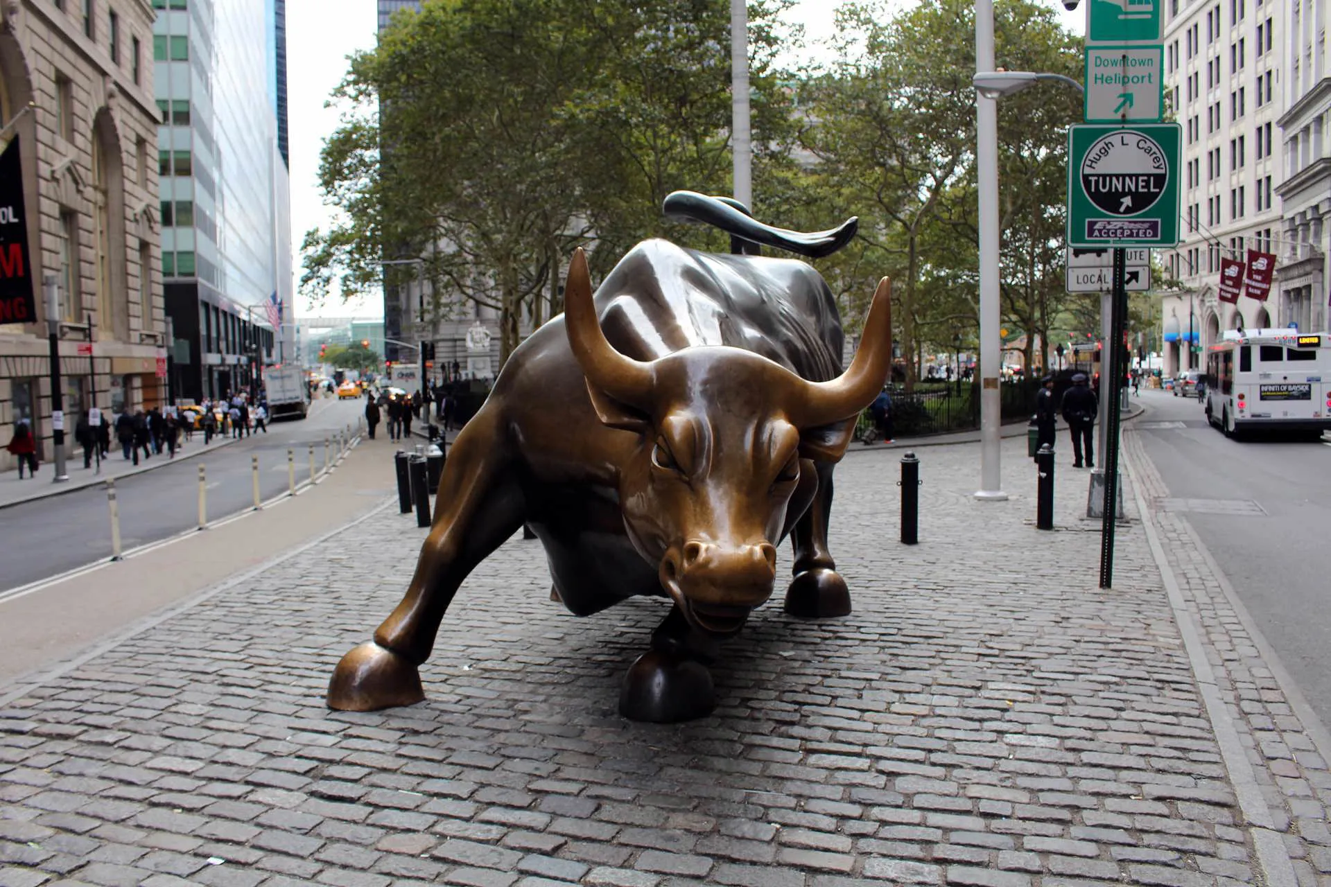A bull statue on a cobbled path in the New York City Finance District with trees behind.