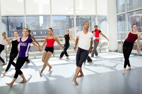 Dancers wearing gym clothing performing a dance in a white windowed room.