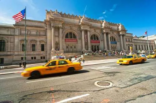 Yellow cabs driving past a sandy coloured pillared building in NYC.