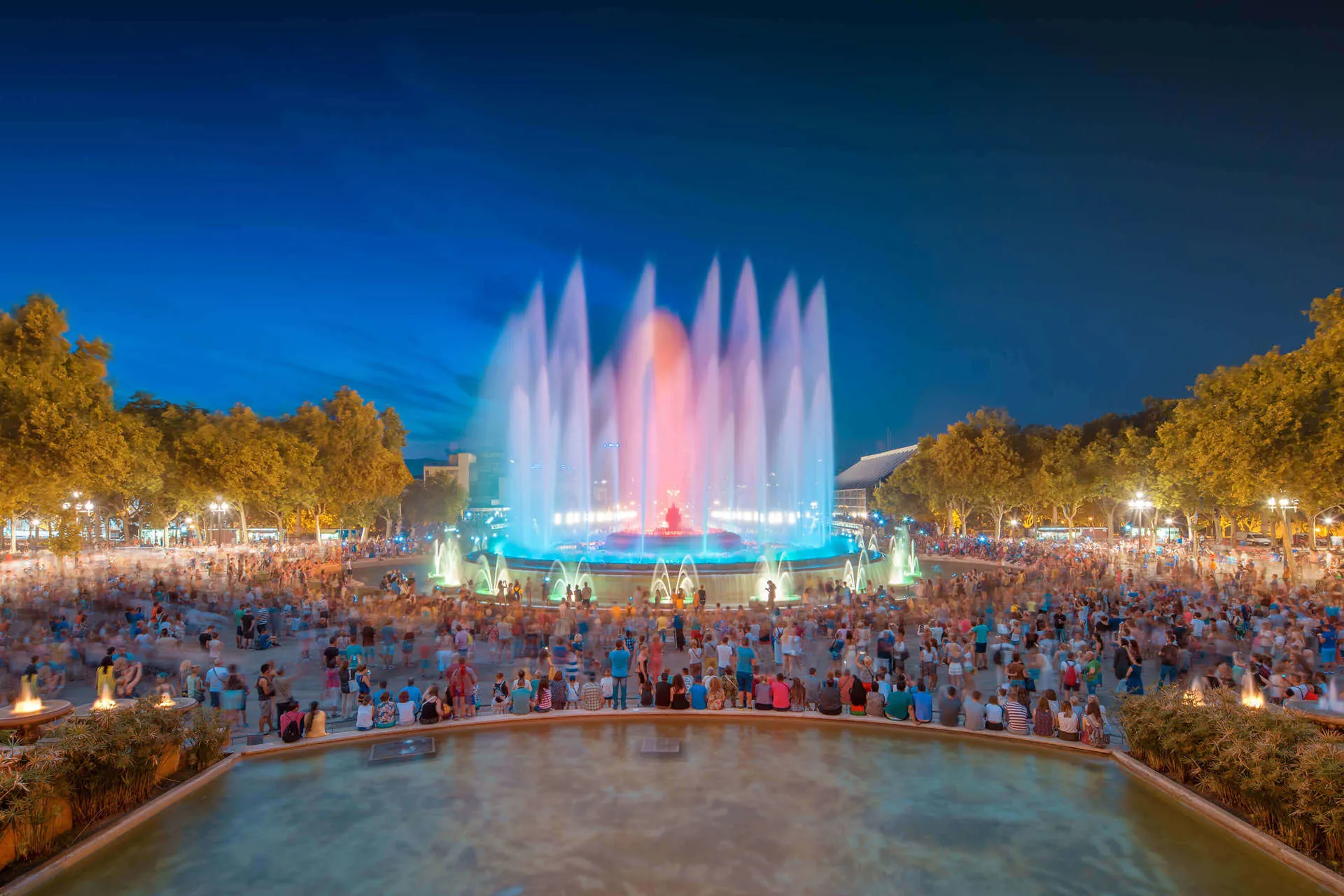 Tourists watch a fountain show in the centre of Barcelona, as it lights up pink, orange and blue at an evening show.