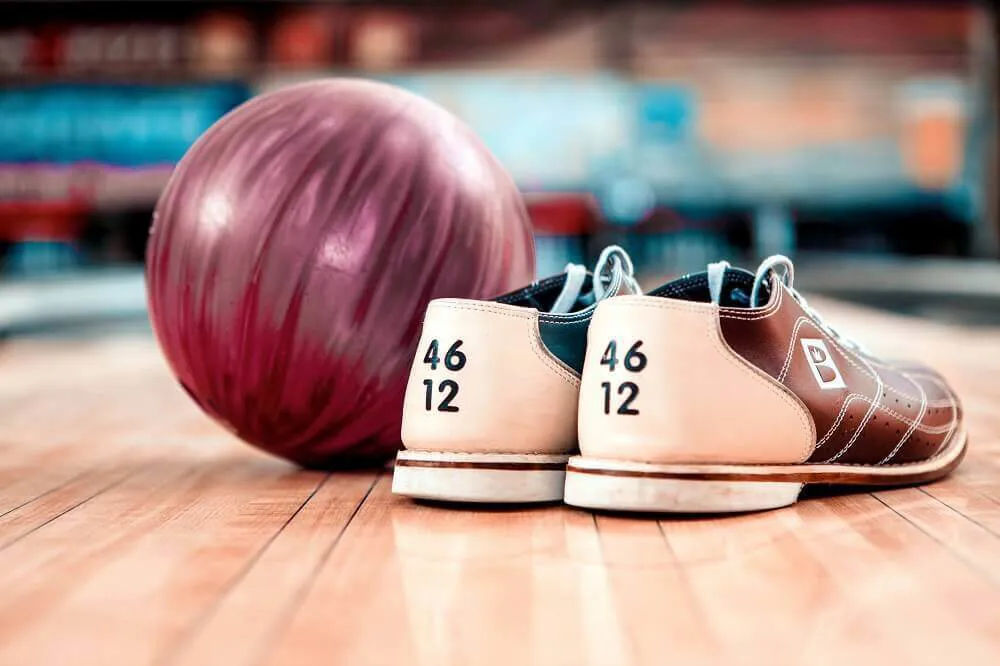 A pair of bowling shoes next to a pink bowling ball on a bowling alley.