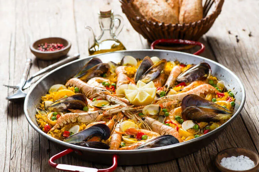 A dish of seafood paella, surrounded by bread and spices.
