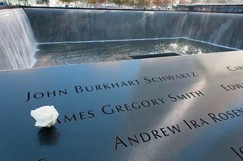 The 9/11 Memorial with a plaque of victims and a white rose placed on it.